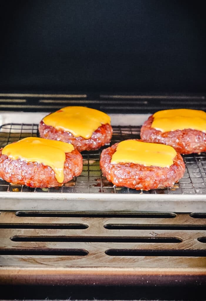 cheddar cheese melting on pork burgers in a smoker