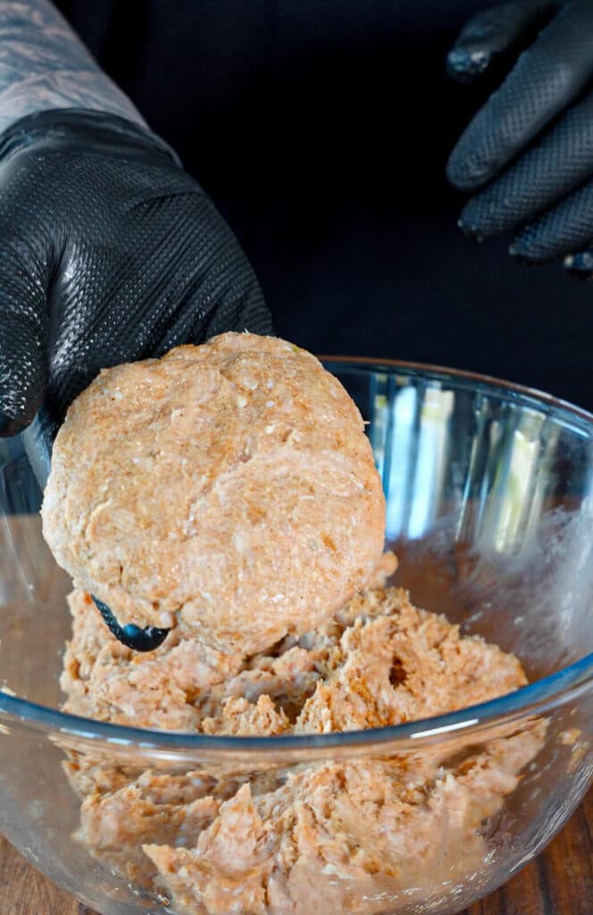 ground chicken patty formed in a hand with a black glove