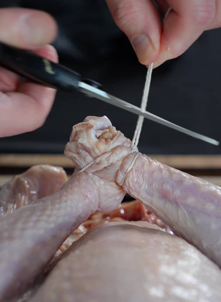 scissors cutting butchers twine that is tying two turkey legs together.