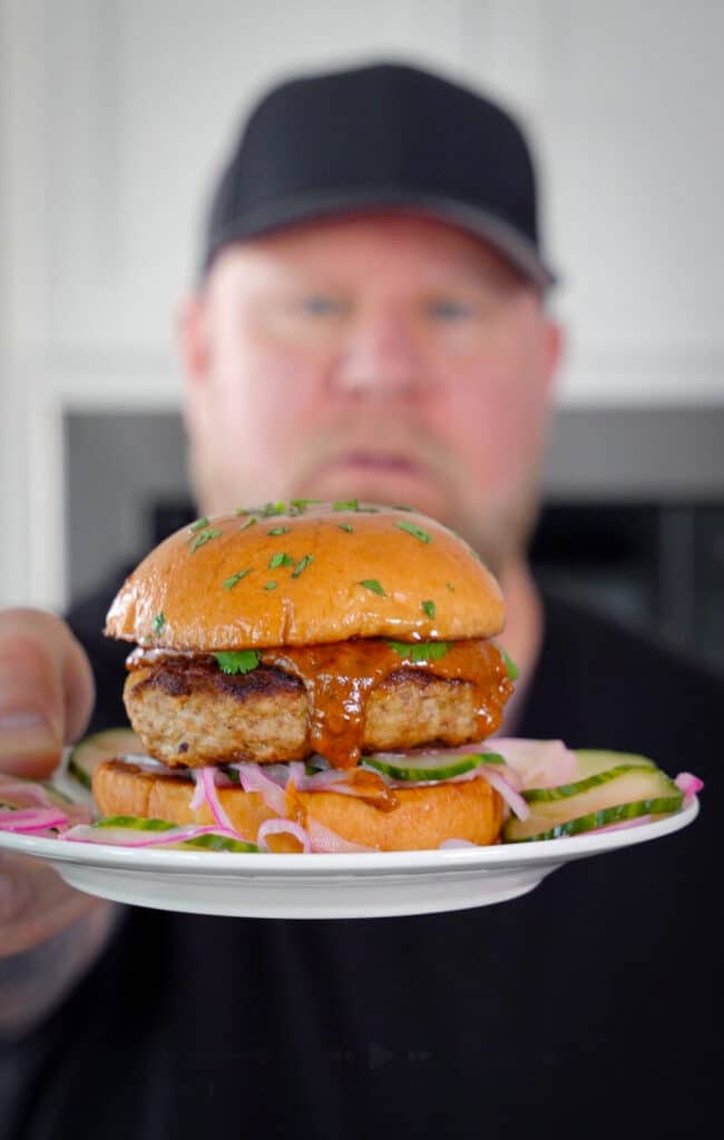 holding an Indian butter chicken burger on a white plate