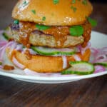indian butter chicken burger sitting on a white plate