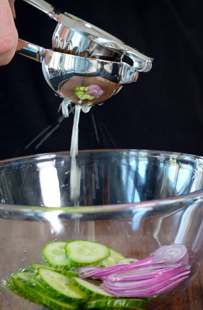 lemon juice going into a bowl with cucumbers