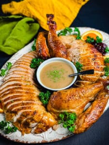 smoked turkey that's been sliced up and placed on a platter with a bowl of gravy