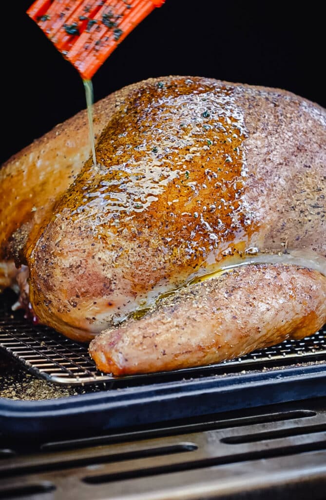 turkey breast being basted with melted butter inside of a smoker