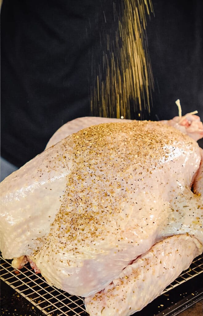 turkey seasoning blend being sprinkled over a whole uncooked turkey