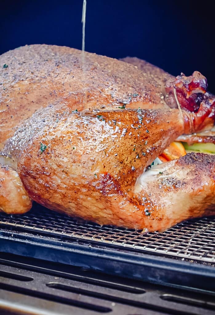 basting a turkey leg with melted butter inside of a smoker