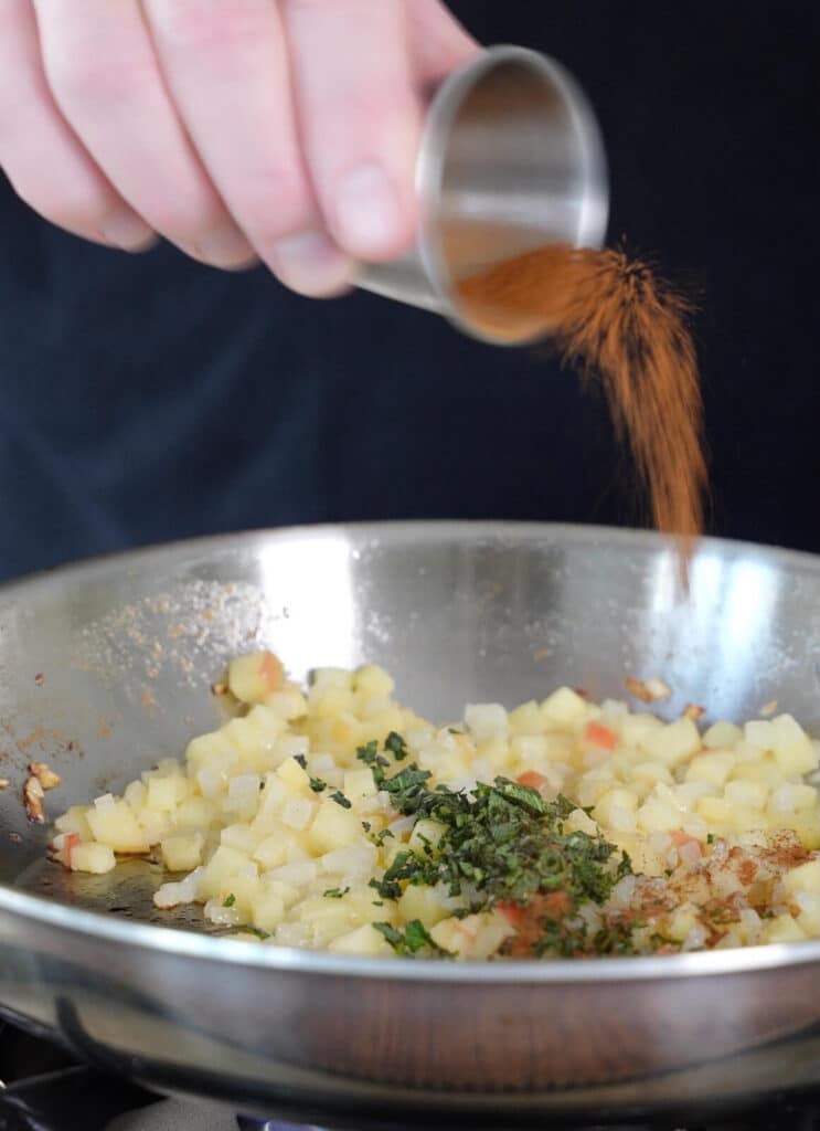 seasoning being added to apples and onions in a skillet