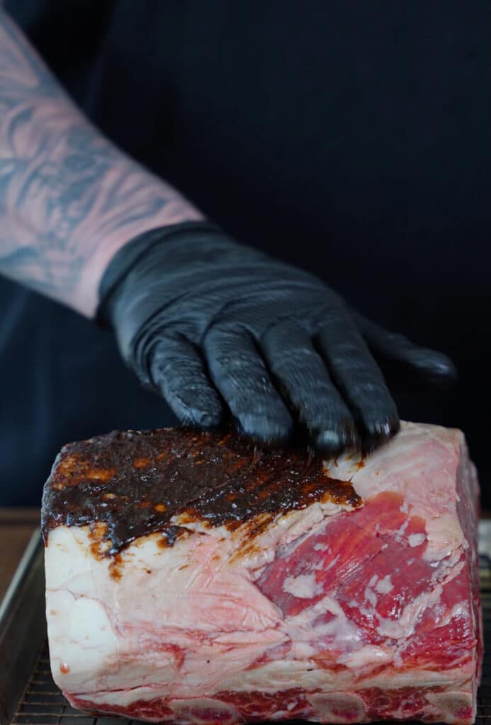 gloved hand spreading beef base on a prime rib roast