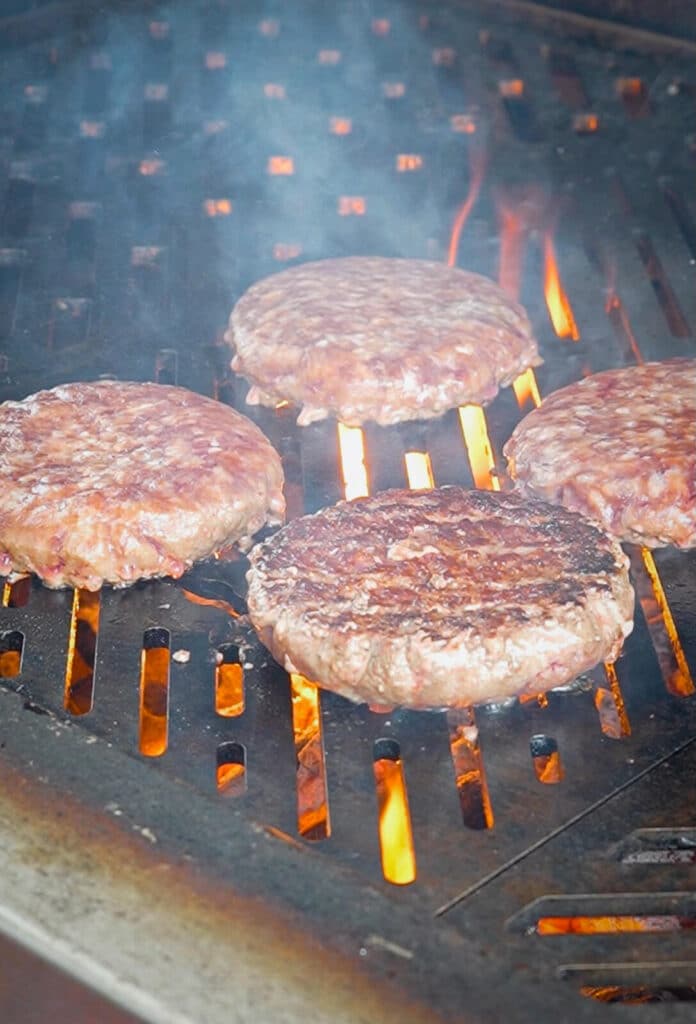 burgers being cooked on a grill over direct heat with flames