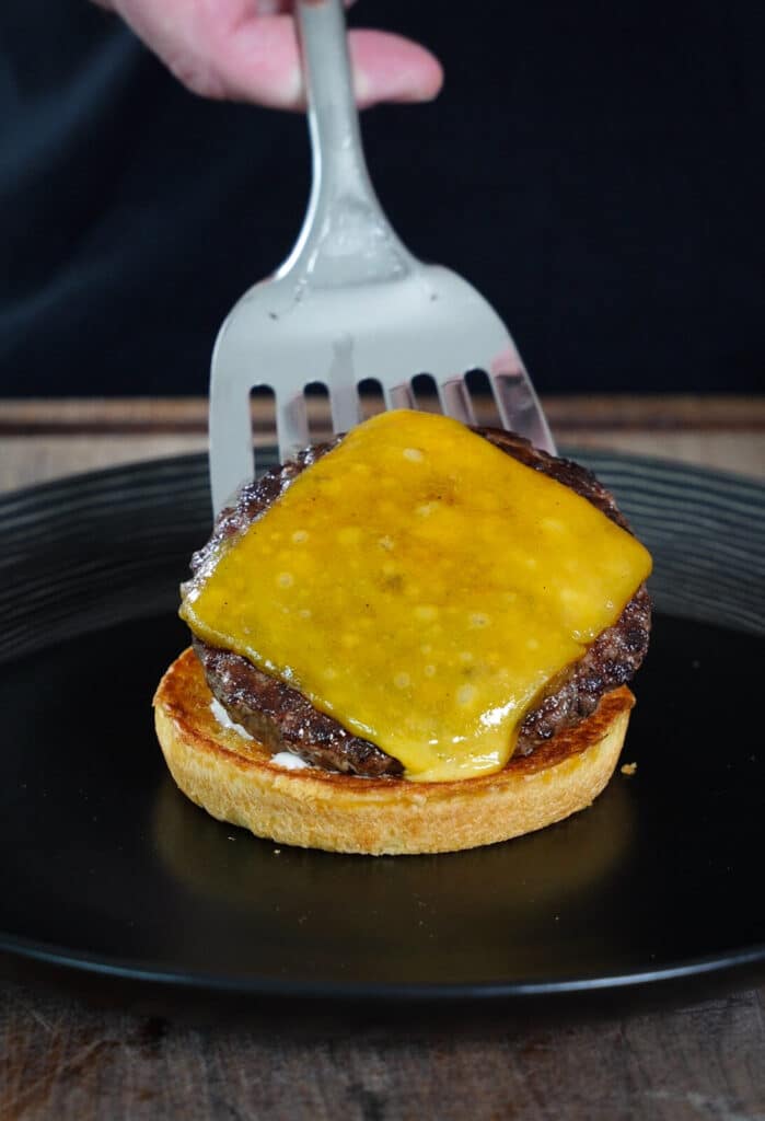 cheese burger patty being added to a bun