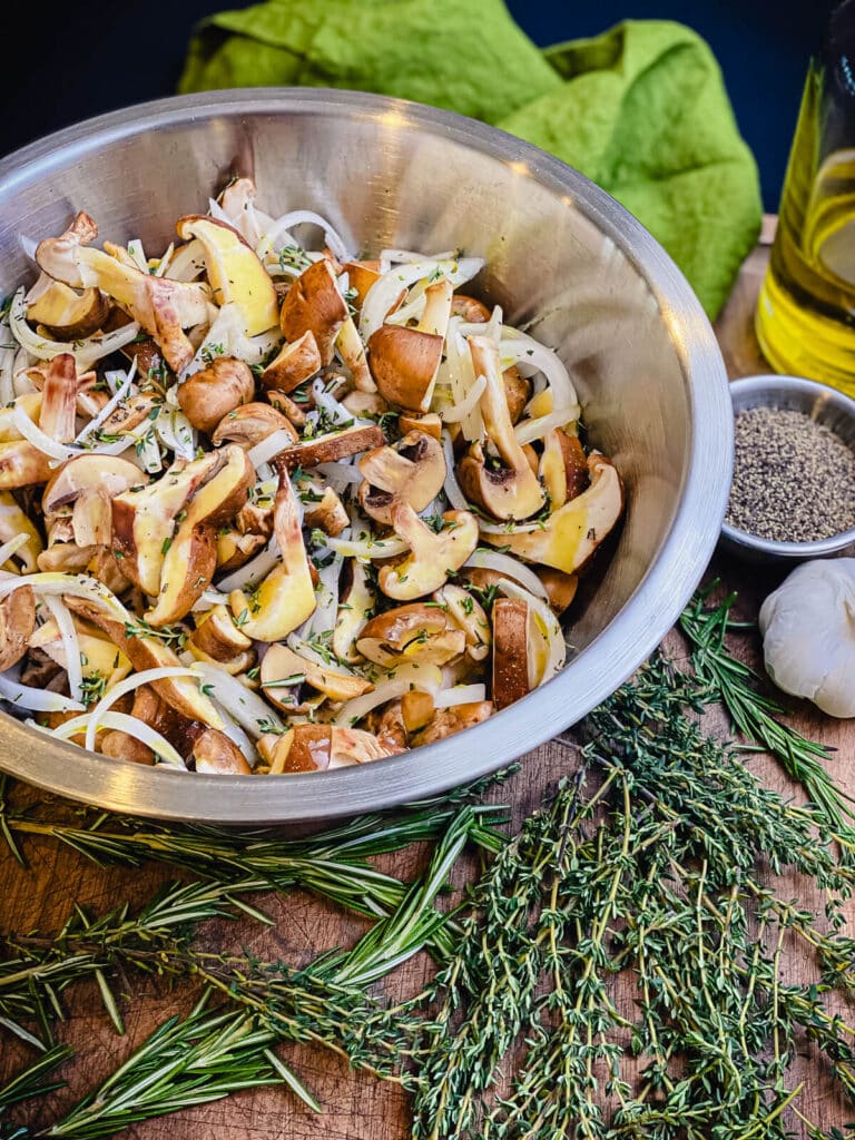 mushrooms and onions drizzled with olive oil and tossed with herbs in a bowl