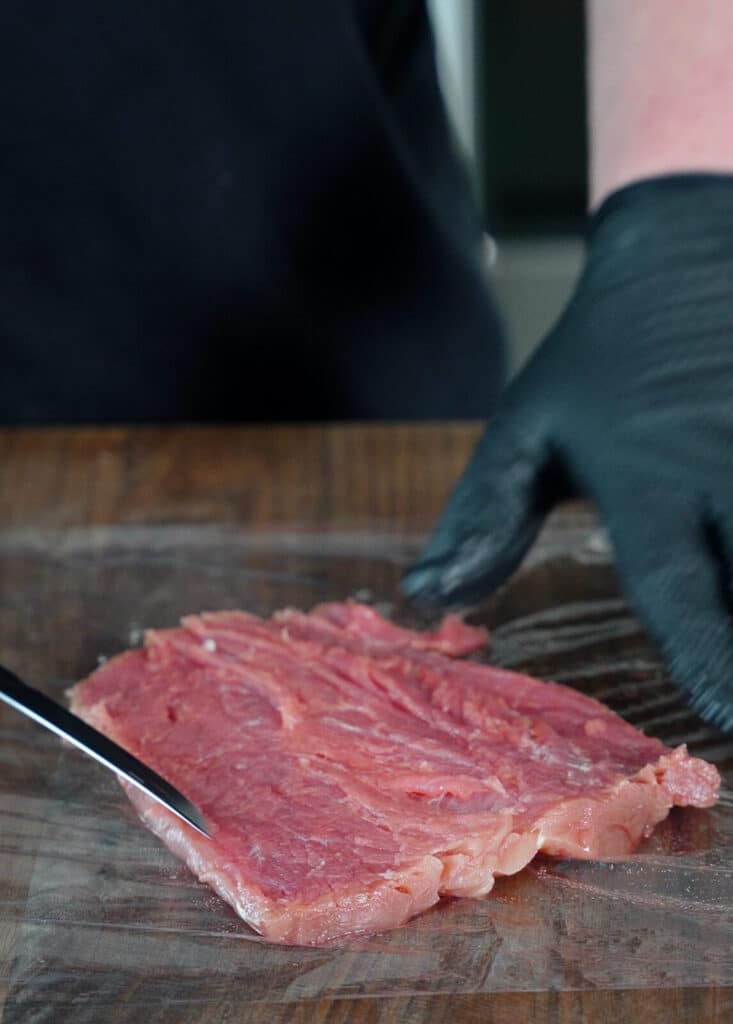 flat pork tenderloin on a sheet of plastic wrap