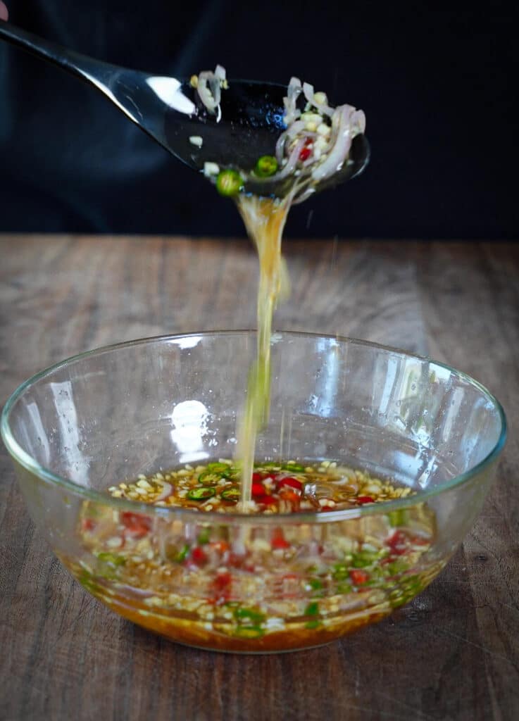 prik nam pla being poured out of a spoon into a glass bowl