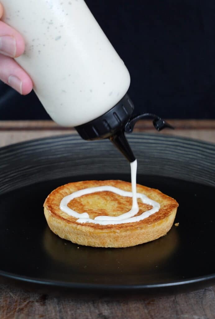 bbq ranch dressing being added to a bottom toasted burger bun