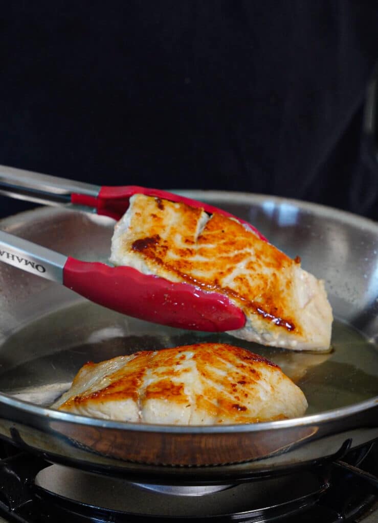 seared red snapper being flipped in a pan with avocado oil