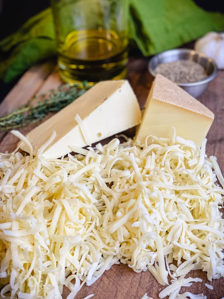 shredded cheeses on a cutting board with olive oil and herbs