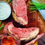 sliced, smoked prime rib on a wood cutting board with chives and horseradish sauce
