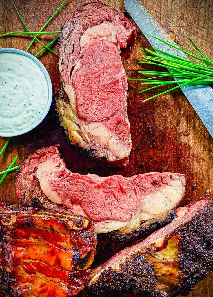 sliced, smoked prime rib on a wood cutting board with chives and horseradish sauce