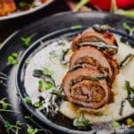 sliced stuffed pork tenderloin on a blue plate with herbs