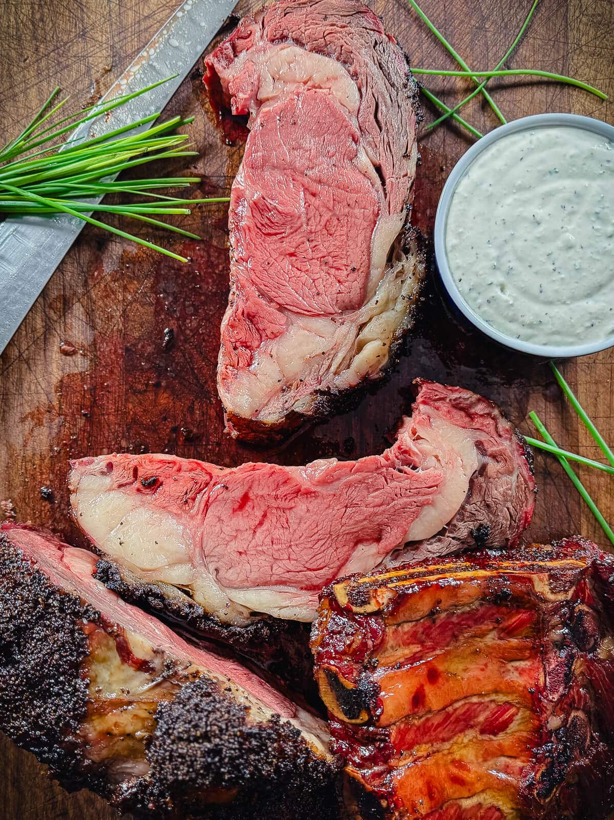 smoked prime rib roast on a cutting board with chives and horseradish sauce