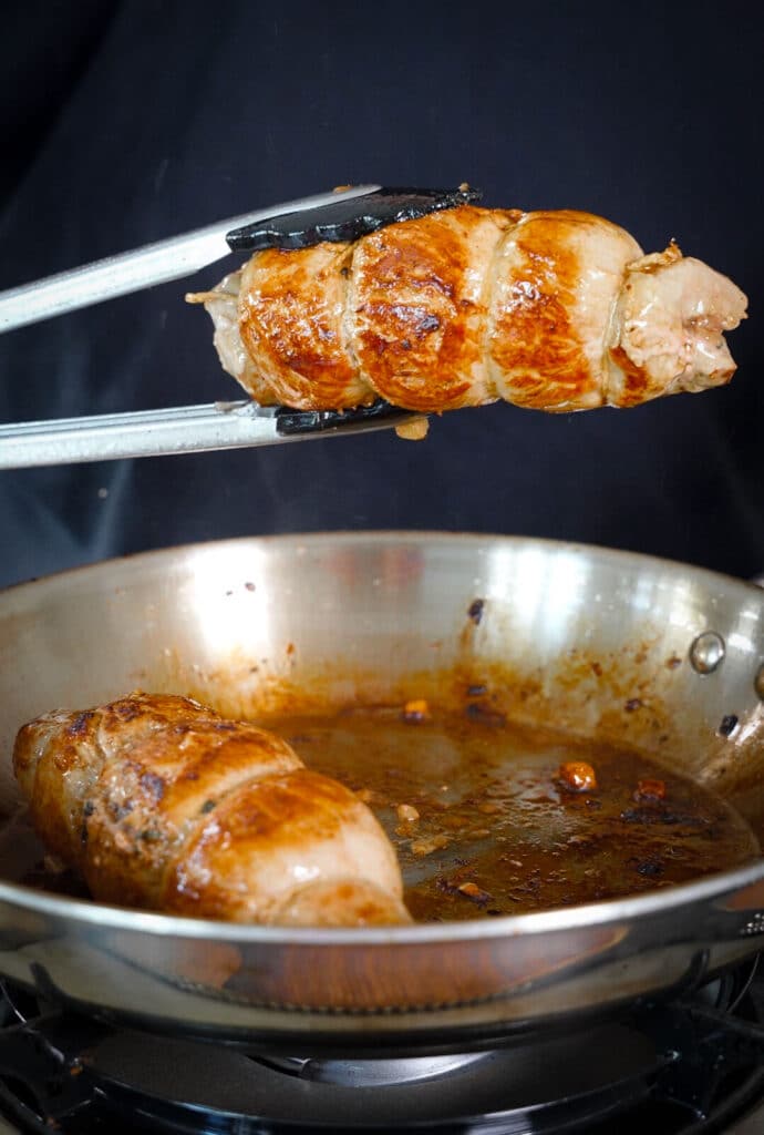 seared stuffed pork tenderloin being held by tongs over a pan