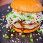 kung pao chicken burger on a plate with scallions and peanuts