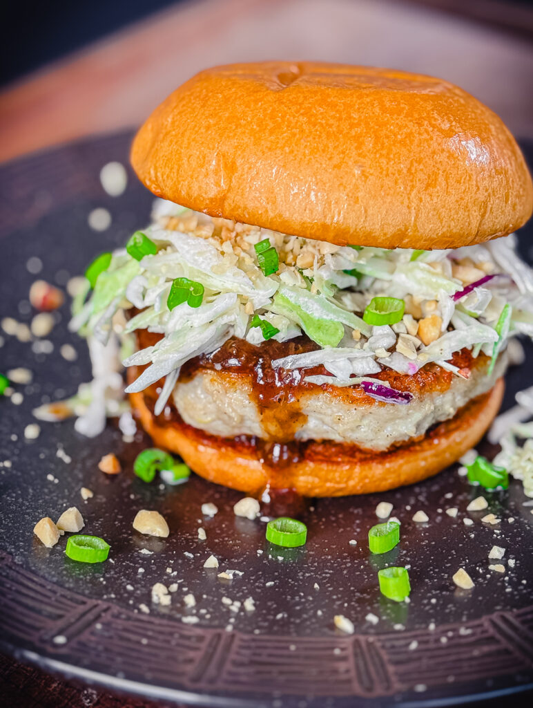 kung pao chicken burger on a plate with scallions and peanuts