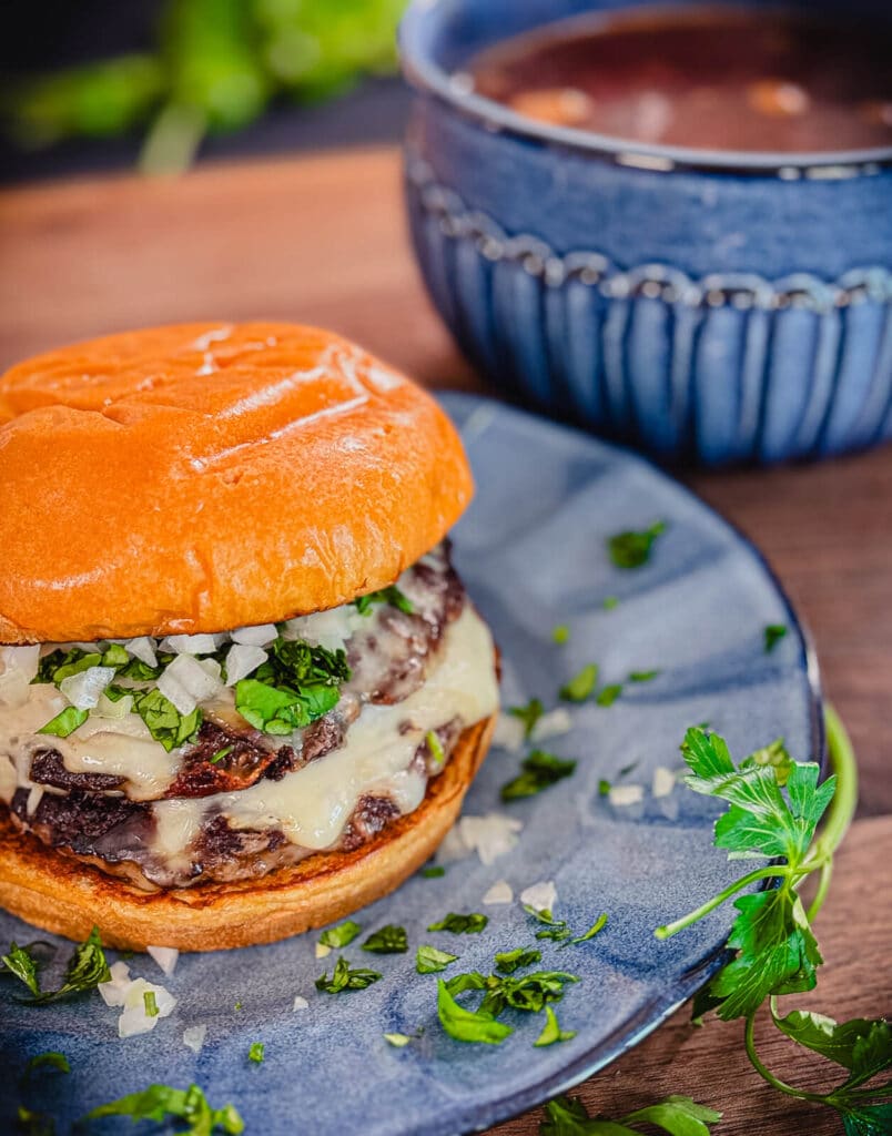 birria smashburger sitting on a blue plate with a bowl of consomme