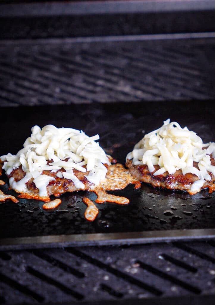 burgers on a griddle with a pile of cheese on each one