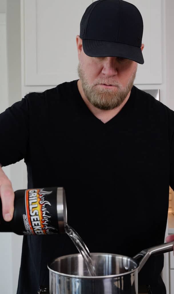 pouring water into a saucepan with birria base