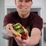man holding a seattle style hot dog with jalapenos