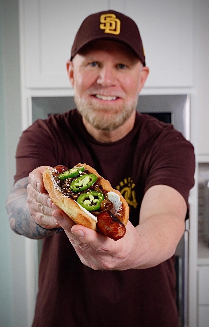man holding a seattle style hot dog with jalapenos