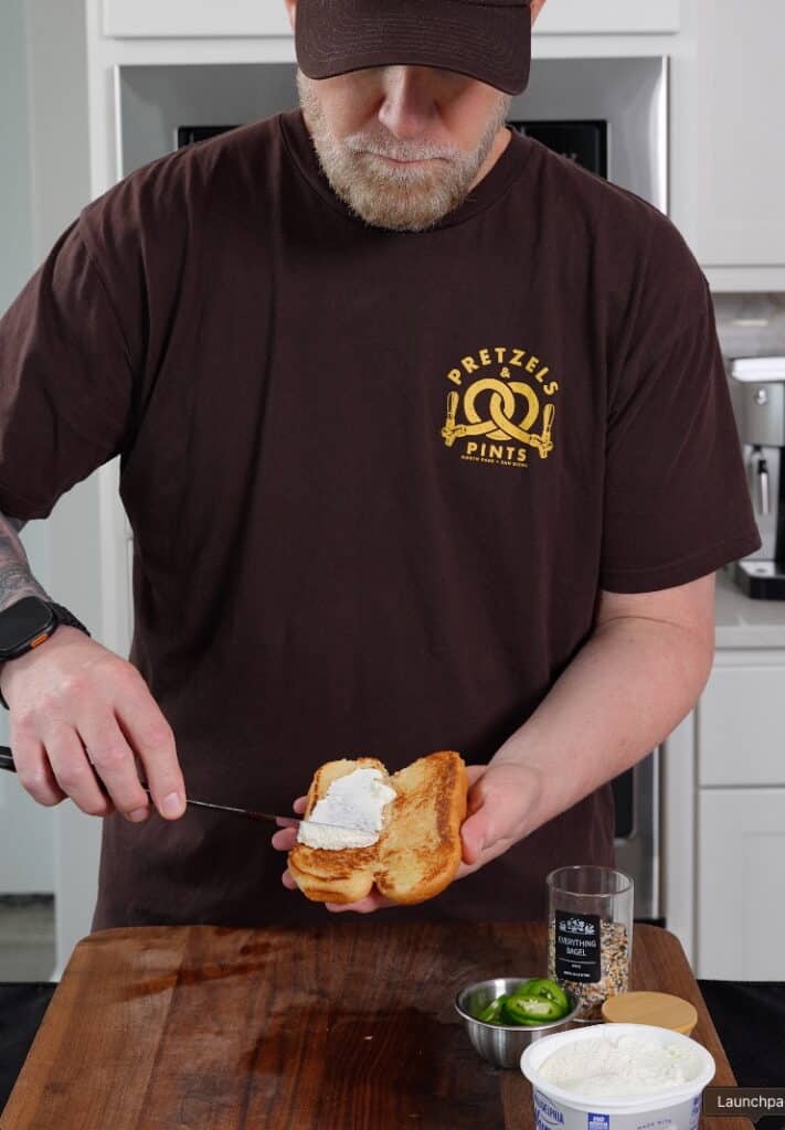 cream cheese being applied to a hot dog bun for a seattle style hot dog