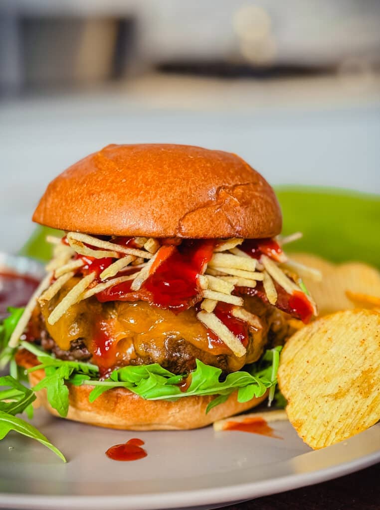 venison burger with bacon and cheery bbq sauce on a plate with potato chips