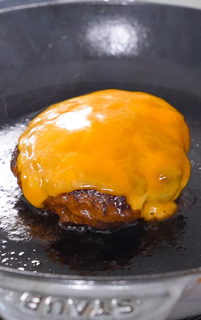 melted smoked cheddar cheese on a venison burger in a cast iron pan