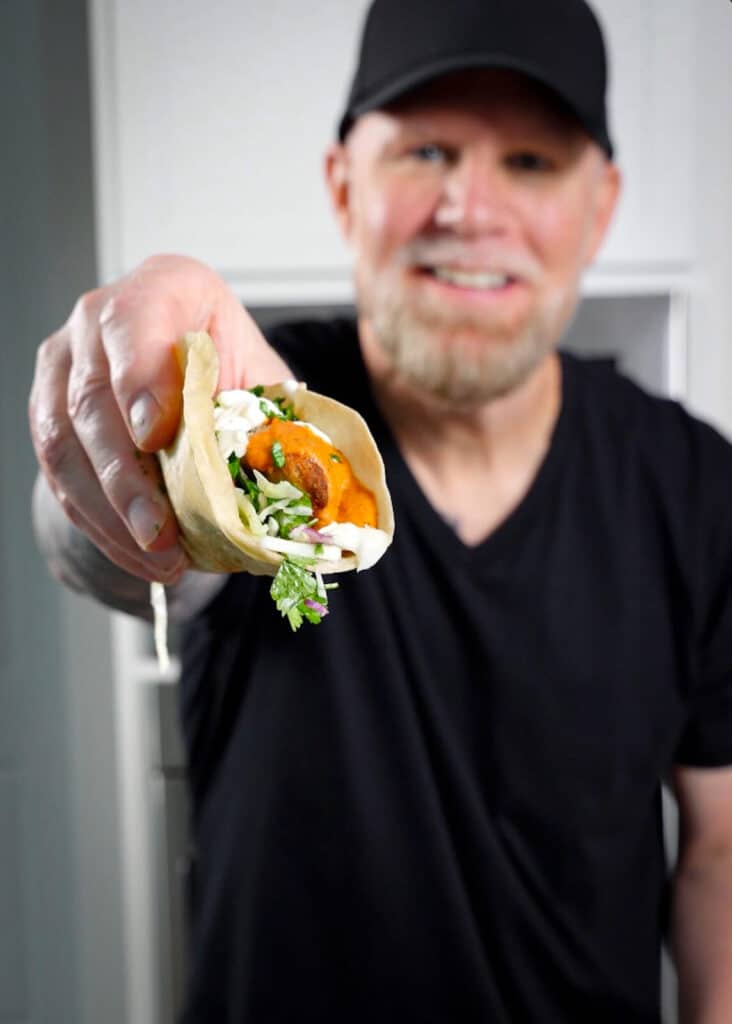 man in a black tee shirt holding a taco for the camera