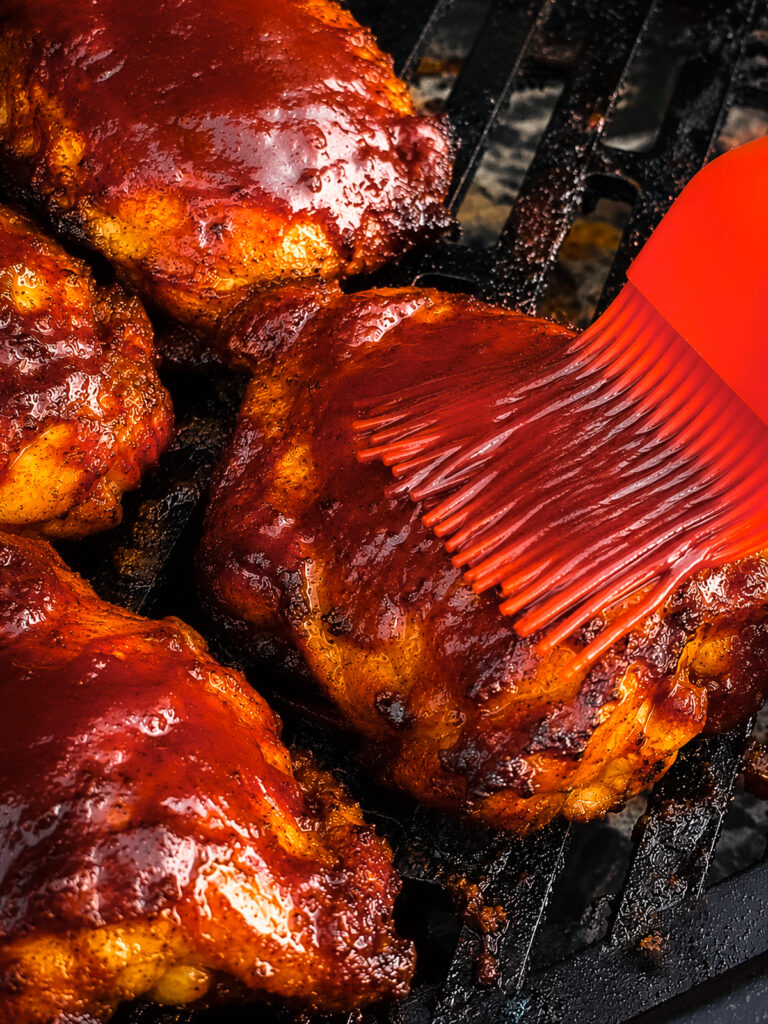 hot honey bbq sauce being basted on a chicken thigh on a grill