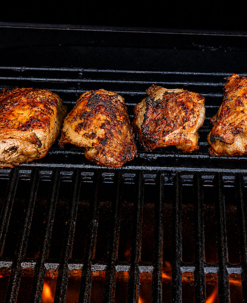 grilled chicken thighs on a warming rack on a grill