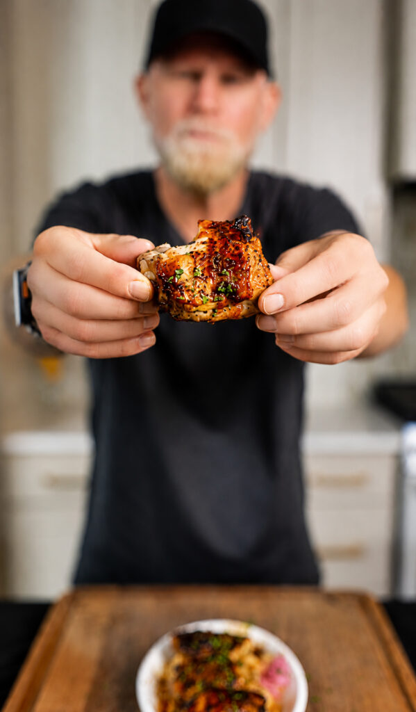 man holding a chicken thigh that has a bite taken out of it
