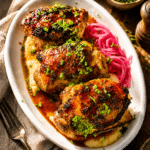grilled hot honey chicken thighs on a plate of polenta with pickled red onions