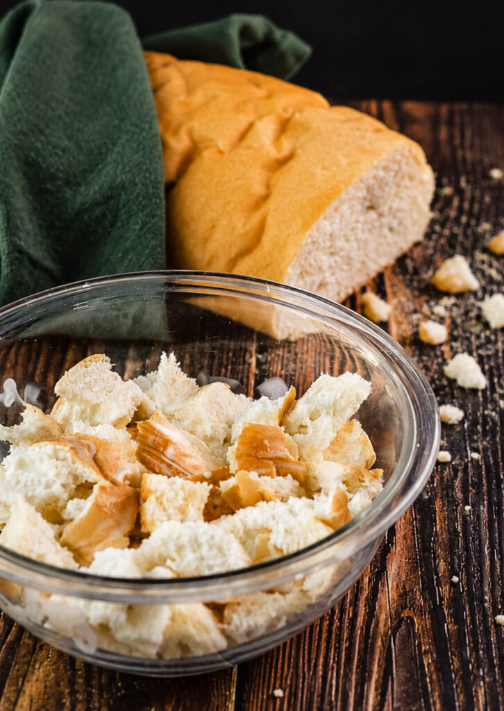 chunks of Italian bread being soaked in buttermilk in a glass bowl