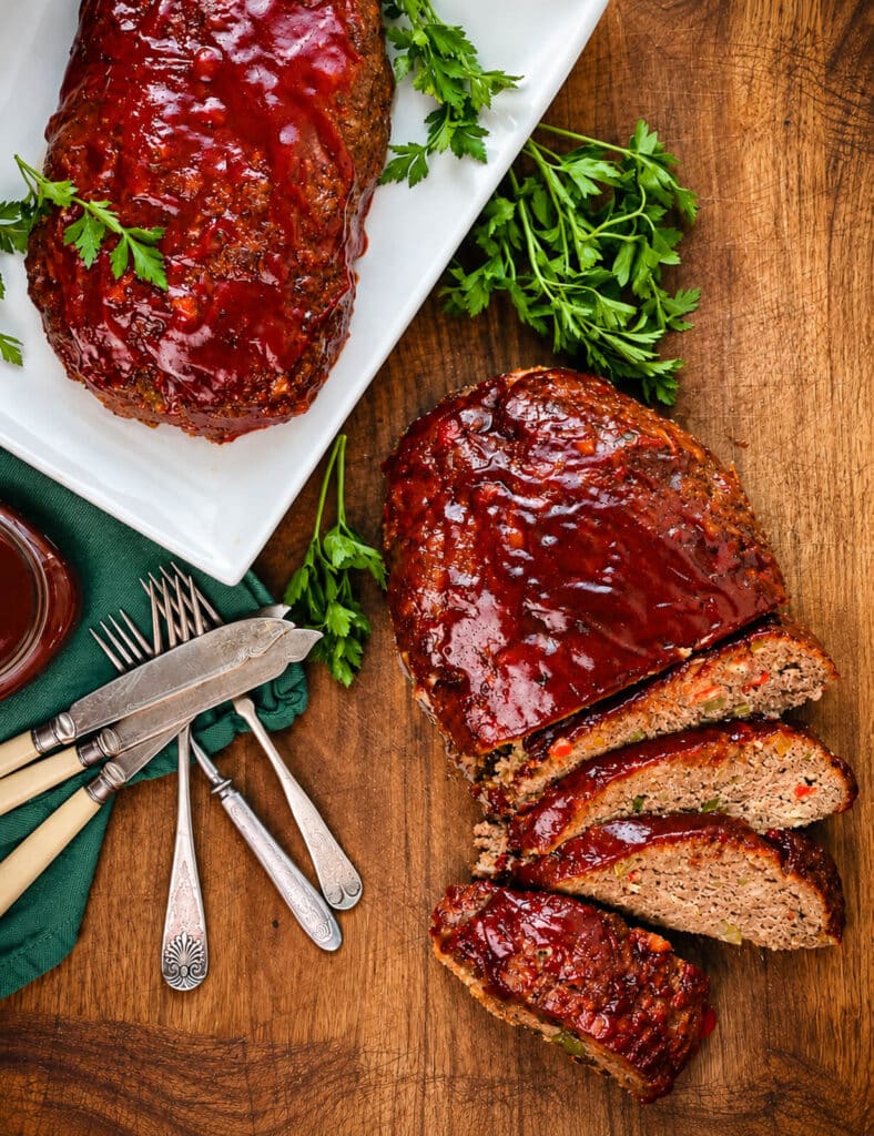 sliced Italian meatloaf, glazed with sauce, sitting on a wood cutting board