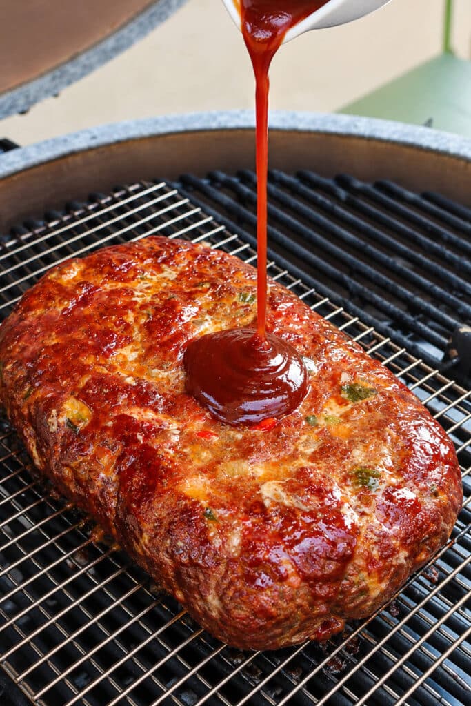tomato sauce being poured onto a grilled meatloaf on a grill