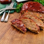 sliced meatloaf on a wood cutting board with a jar of meatloaf glaze in the background