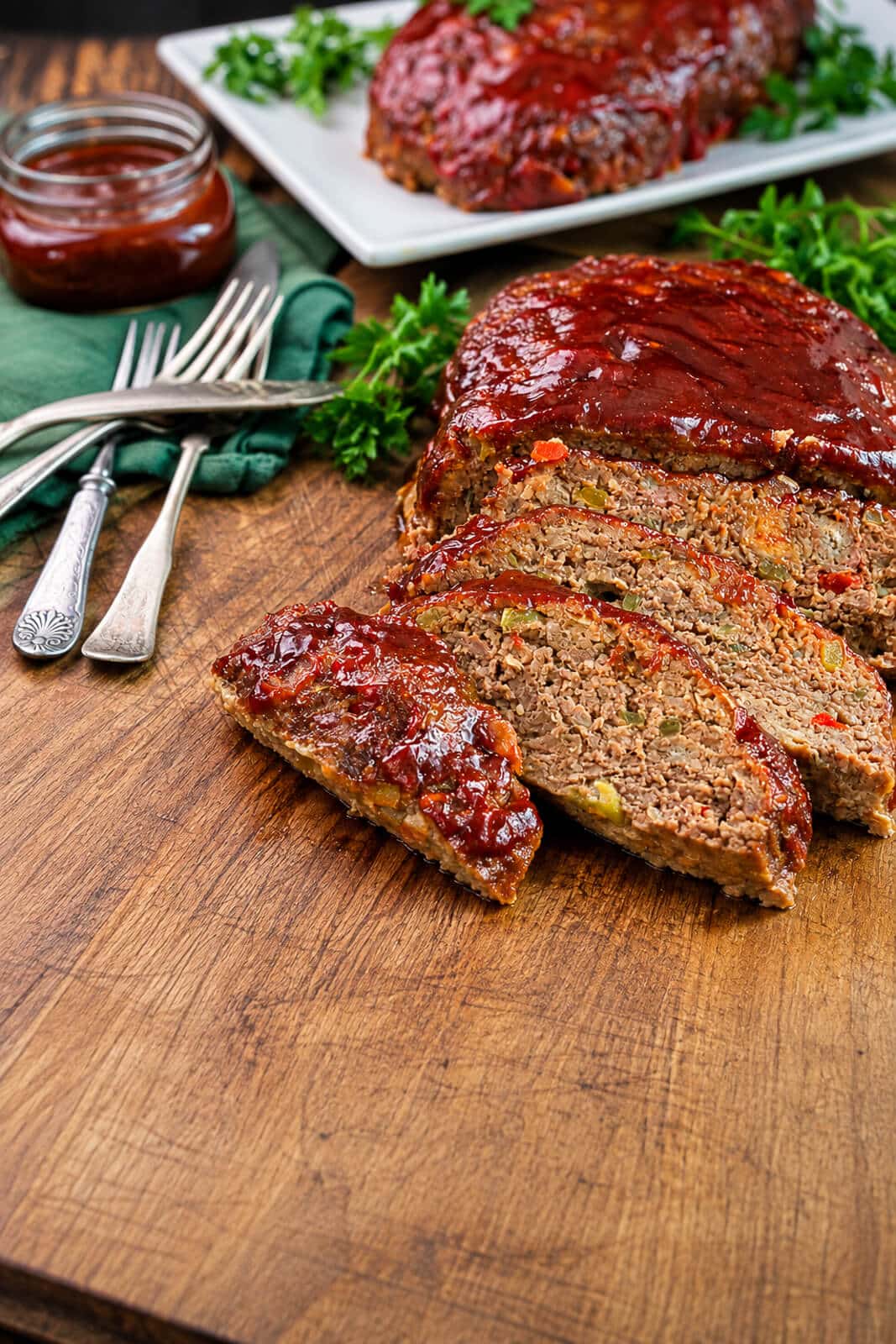 sliced meatloaf on a wood cutting board with a jar of meatloaf glaze in the background