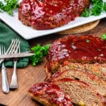 sliced Italian meatloaf on a wood cutting board with a green towel