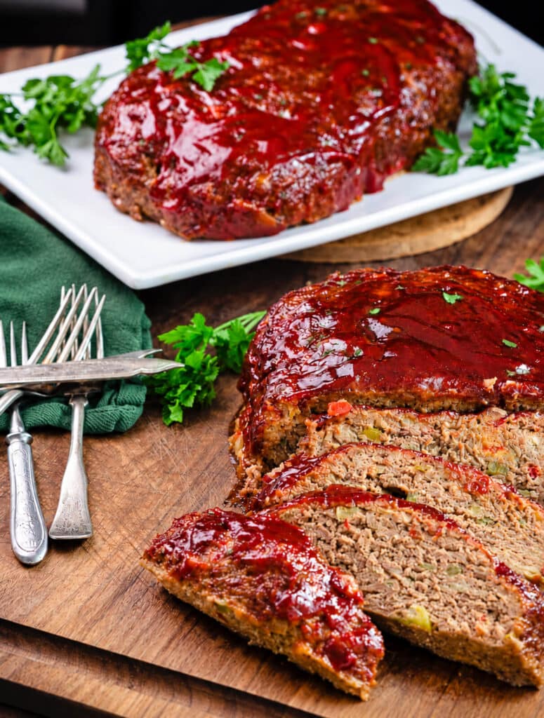 sliced Italian meatloaf on a wood cutting board with a green towel