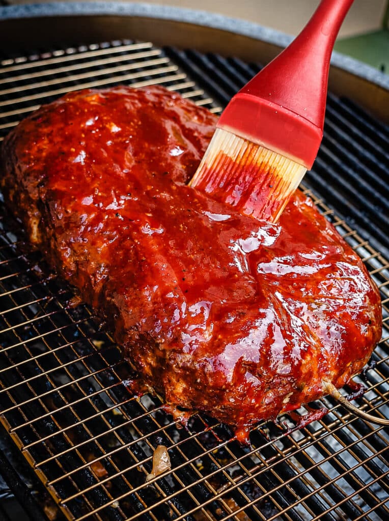 sauce being brushed onto meatloaf on a grill