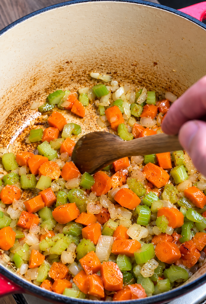 wooden spoon mixing veggies in a Dutch oven